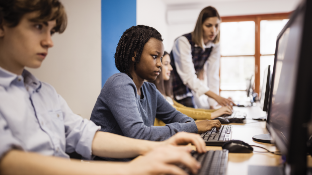 Teacher assisting high school students using computers in a computer lab